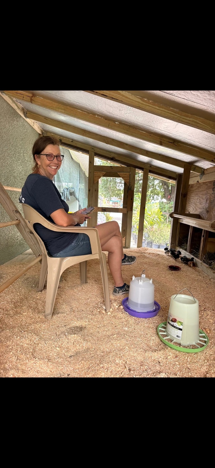 A smiling woman spending time with the chicks in the farm coop