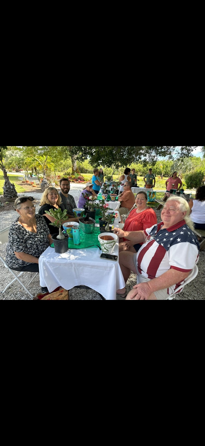 Smiling guests seated around an outdoor table with desert roses and colorful pots